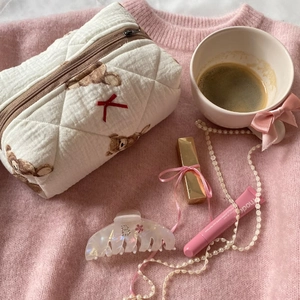 Quilted cotton teddy bear makeup bag with red bow on a pink knit sweater backdrop