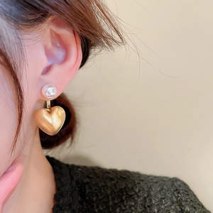 Close-up of pearl stud earrings with matte gold heart pendants on a model