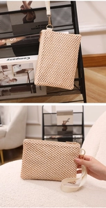Detail of hollow woven straw beach wristlet bag with beige fabric handle and metal zipper
