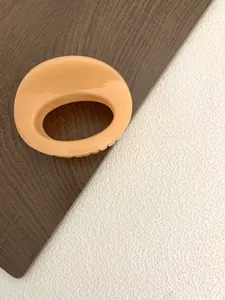 Detail of a light orange oval hair claw clip with a glossy finish on a wooden texture