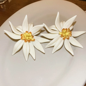 Macro view of white resin floral earrings with yellow beaded centers on a white plate