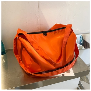 Detail of a bright orange large oxford shoulder bag on a metallic finish surface