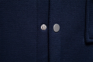 Detail of waffle knit fabric texture and metal snap button on navy blue cardigan jacket