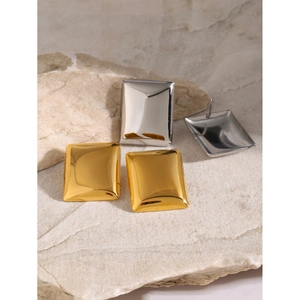 Detailed macro view of gold and silver rectangular geometric stud earrings on natural rock