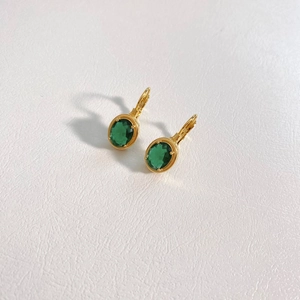 Detail of gold-plated stainless steel earrings with oval green zircon on beige leather