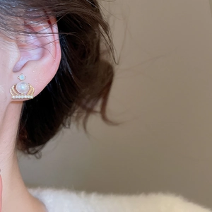 Close-up of crown-shaped gold pearl stud earring with sparkling zircon on ear