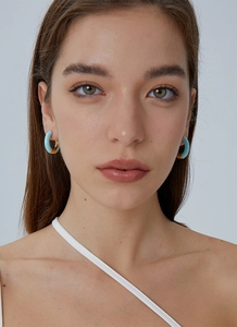 Detailed view of elegant blue and gold enamel C-shaped earrings worn by a model