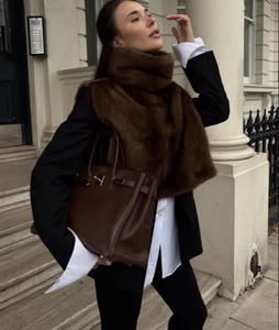 Dettaglio di un gilet in ecopelliccia marrone scuro con borsa in pelle coordinata in città
