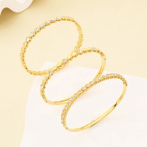 Vue détaillée de trois bracelets joncs dorés sertis de zircons sur un support blanc