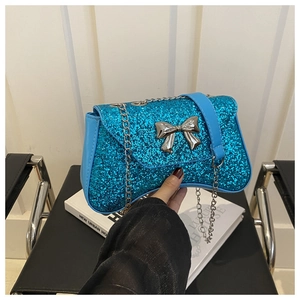 Detail of blue sequin handbag with silver bow accent and metal chain strap held by hand