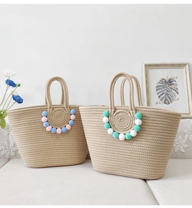Detail of handmade straw tote bags with decorative colorful pom-poms on a white sofa