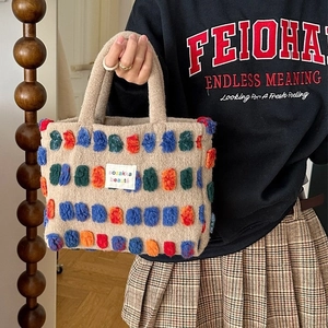 Oatmeal plush bucket bag with colorful tufted dots and branded label held by a model