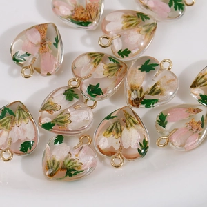Heart resin pendants with pink dried flowers and green leaves on a white background