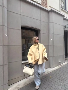 Outdoor street shot of women's yellow wool coat paired with denim and a canvas bag