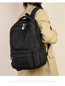 Side view of a large black travel backpack worn by a model in a khaki trench coat