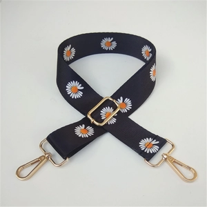 Detail of adjustable wide bag strap featuring white daisy patterns on black nylon webbing