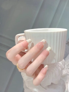 Detail of French tip press-on nails with small pearls and gold beads on ballerina shape