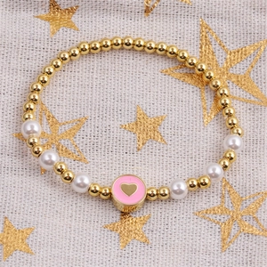 Detailed shot of beaded bracelet with gold beads, pearls and pink heart enamel charm