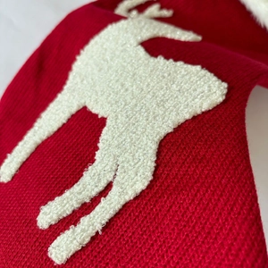 Close-up of red knitted Christmas stocking featuring a white reindeer embroidery detail