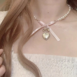 Detail of pearl choker featuring a pink ribbon bow and golden heart pendant on model