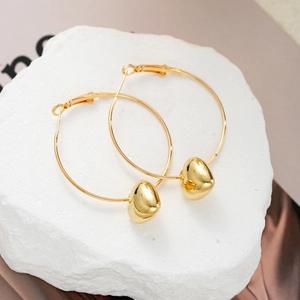 Golden hoop earrings with polished heart pendants on white stone with silk backdrop