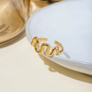 Detail shot of wavy 18k gold plated stainless steel ring on a white ceramic plate