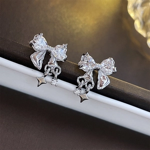 Silver bow stud earrings with zircon star charms shown against a premium jewelry box