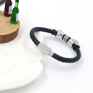 Detail of woven black leather bracelet with silver skull charms and magnetic clasp