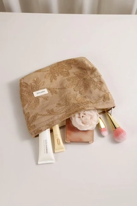 Detailed embroidery of beige floral patterns on a textured cotton linen makeup bag