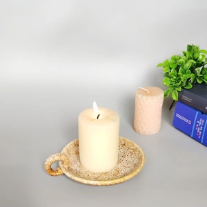 Close-up of beige speckled ceramic candle holder with handle and burning white candle