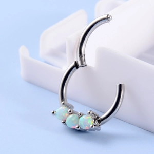 Macro shot of silver hinged hoop ring with three inlaid white opals on blue background