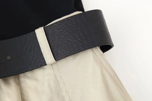 Detail of beige twill fabric with black faux crocodile leather belt on waist