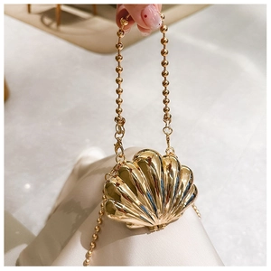Close-up of a golden shell-shaped mini metal bag with a sphere chain held by a hand