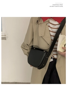 Detail view of a black saddle bag with gold hardware worn with a trench coat