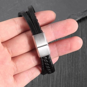 Hand holding a multilayer black braided leather bracelet with a silver magnetic clasp