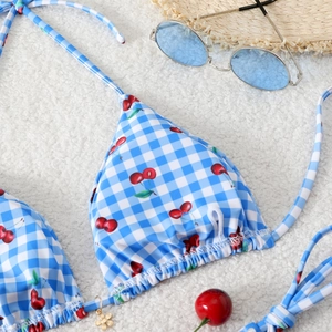 Detail view of blue gingham bikini top with cherry print on white plush background