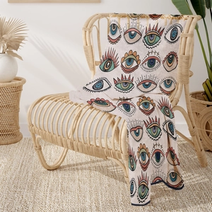 Detail of artistic evil eye flannel throw blanket draped over a bohemian rattan chair