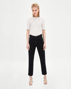 Dettaglio del top in maglia bianca con bordo ondulato nero sulle maniche e scollo