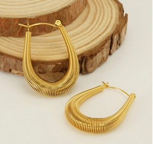 Detailed close-up of gold U-shaped spring coil hoop earrings on a rustic wood background