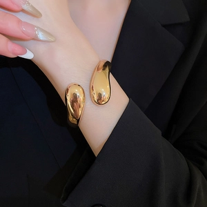 Dettaglio di un bracciale regolabile a goccia d'oro indossato su una manica nera