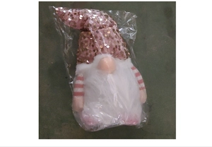 Close-up of pink sequined gnome plush with white fur in protective plastic packaging