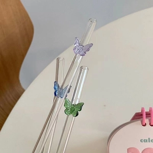 Detail of four transparent glass straws with colored 3D butterflies on a white table