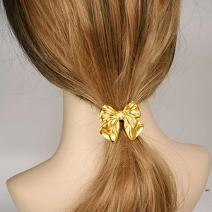 Elegant gold stainless steel bow hair tie accessory worn by model on grey background