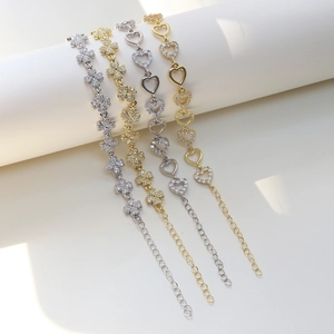 Elegant brass charm bracelet featuring zircon heart and clover patterns on a white pedestal