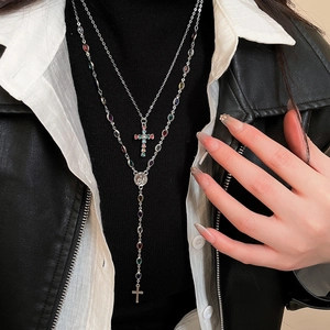 Close-up of a double-layer silver cross necklace with colorful gems and portrait medal