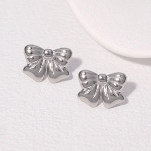 Macro shot of silver bow stud earrings on a minimalist white textured background