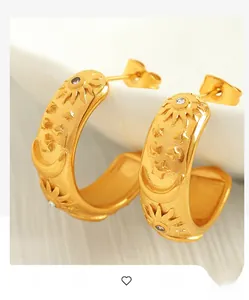 Close-up of gold C-shaped earrings with embossed sun moon star motifs and crystals