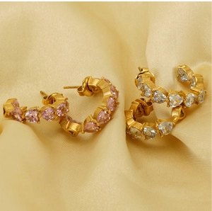 Detailed macro view of U-shaped gold earrings featuring heart-shaped pink and clear zircons