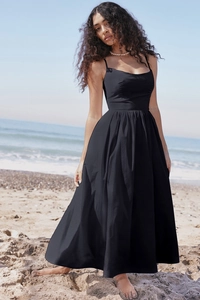 Elegant black backless maxi dress worn by a model on a sunny beach background