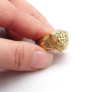 Gros plan détaillé d'une bague bouclier dorée avec relief en croix et motifs ornementaux
